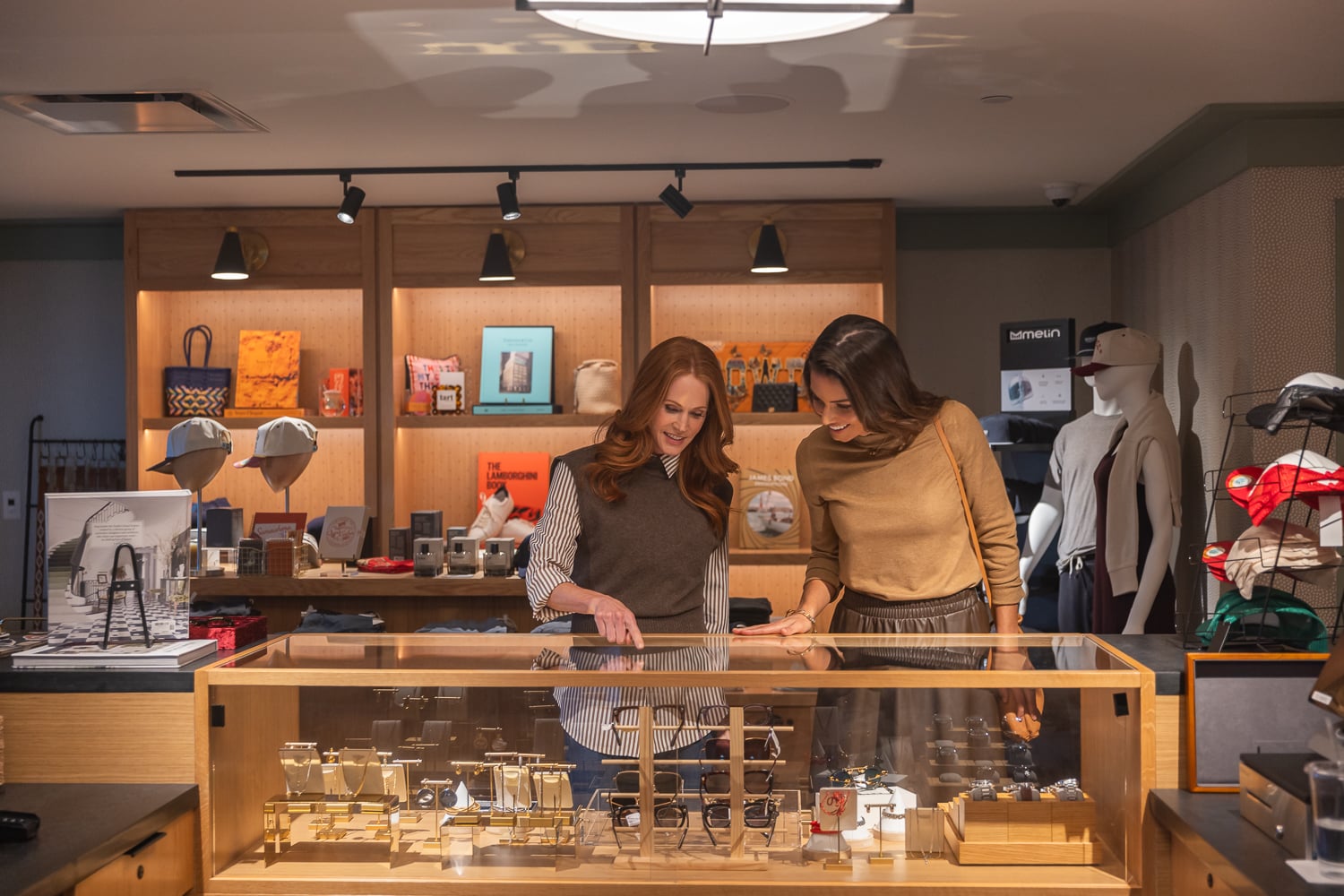 Two smiling women browsing items inside a glass display case at a high-end retail shop.