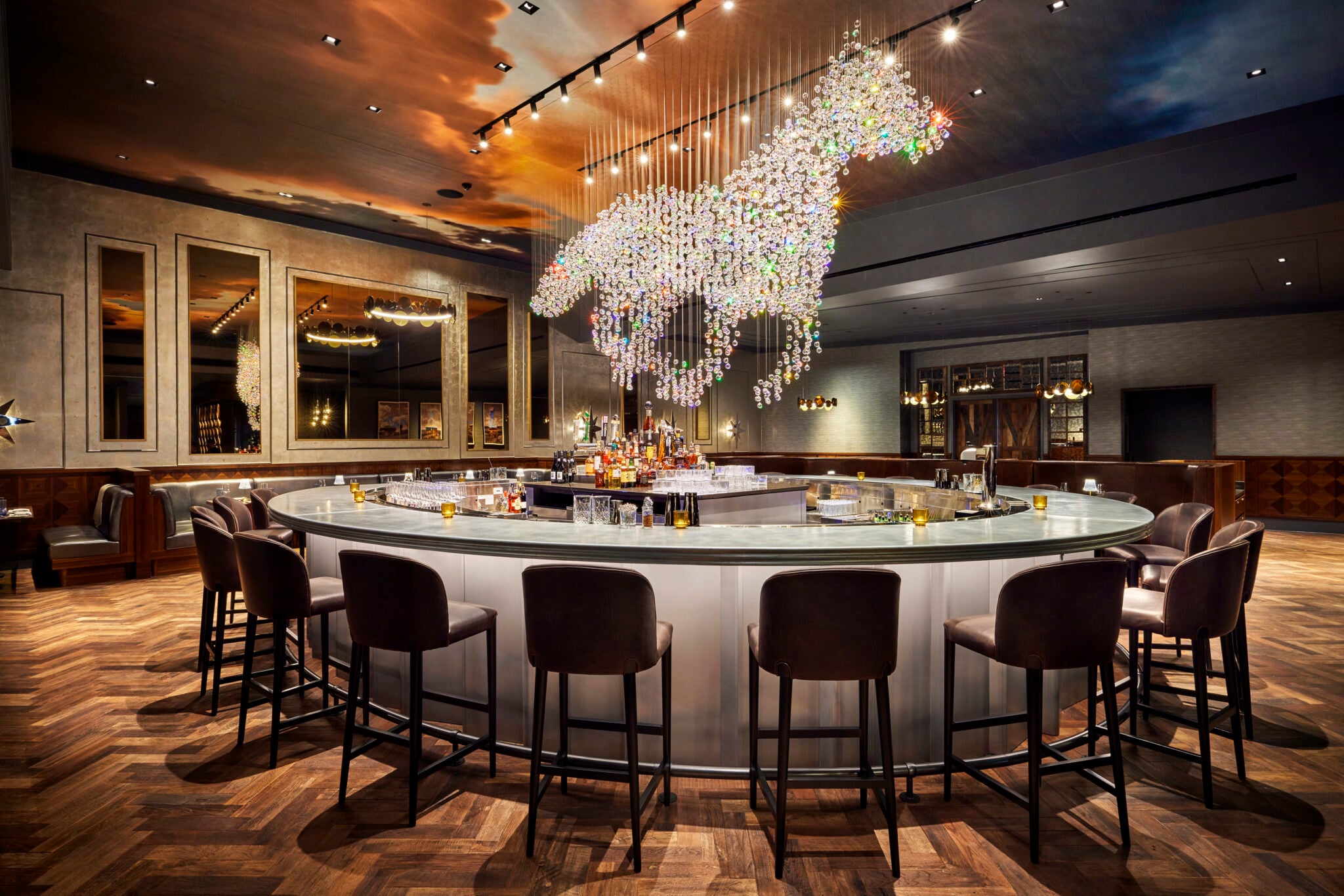A dimly lit bar area with a circular bar and a spectacular, large crystal chandelier shaped like a running horse hanging above.