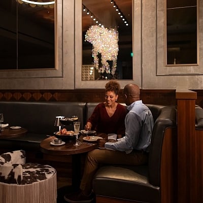 A couple dines in a dark, upscale restaurant booth. The crystal horse chandelier is reflected in the mirror behind them.