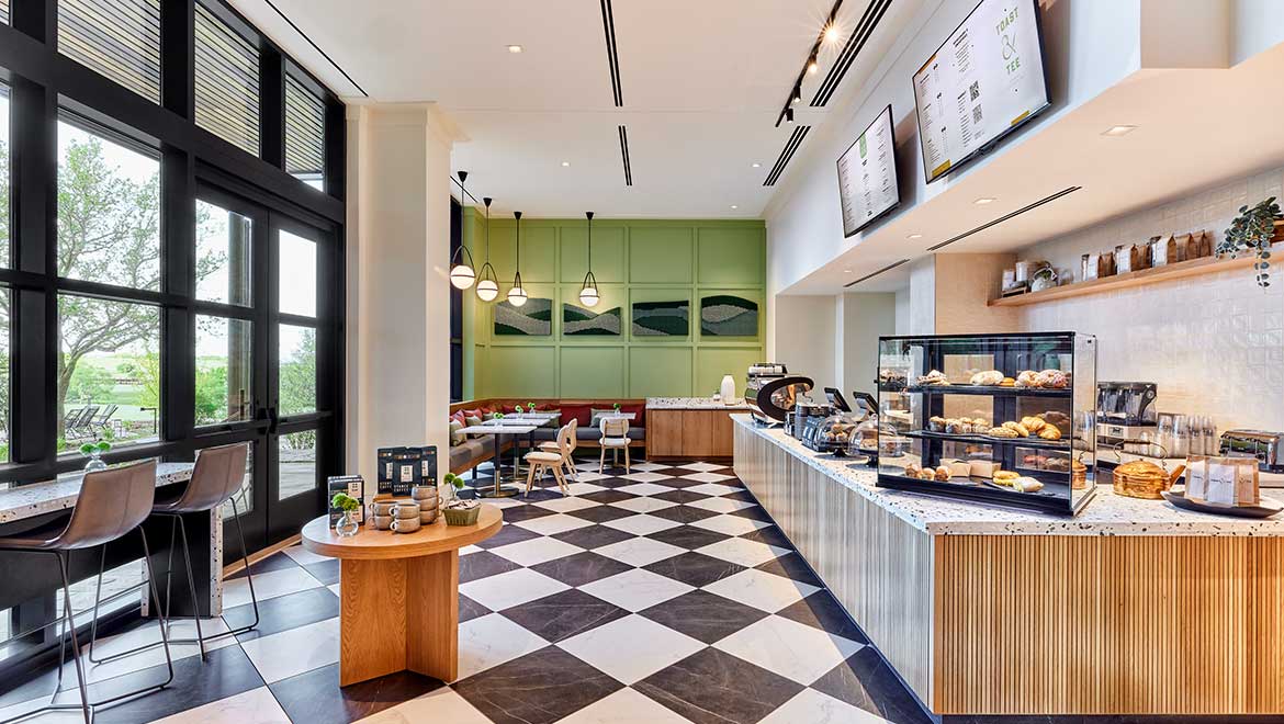 Modern cafe interior with a black and white checkerboard floor, display cases, and tables next to large windows.