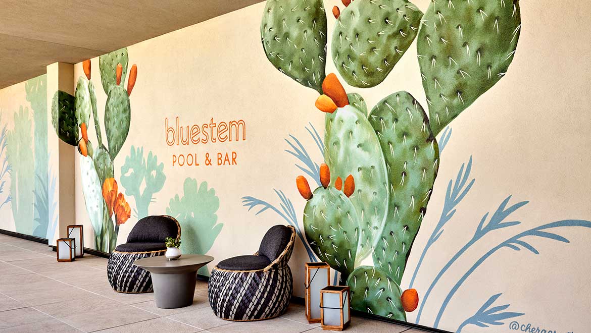 Outdoor lounge area with woven chairs next to a large mural of prickly pear cacti and the 