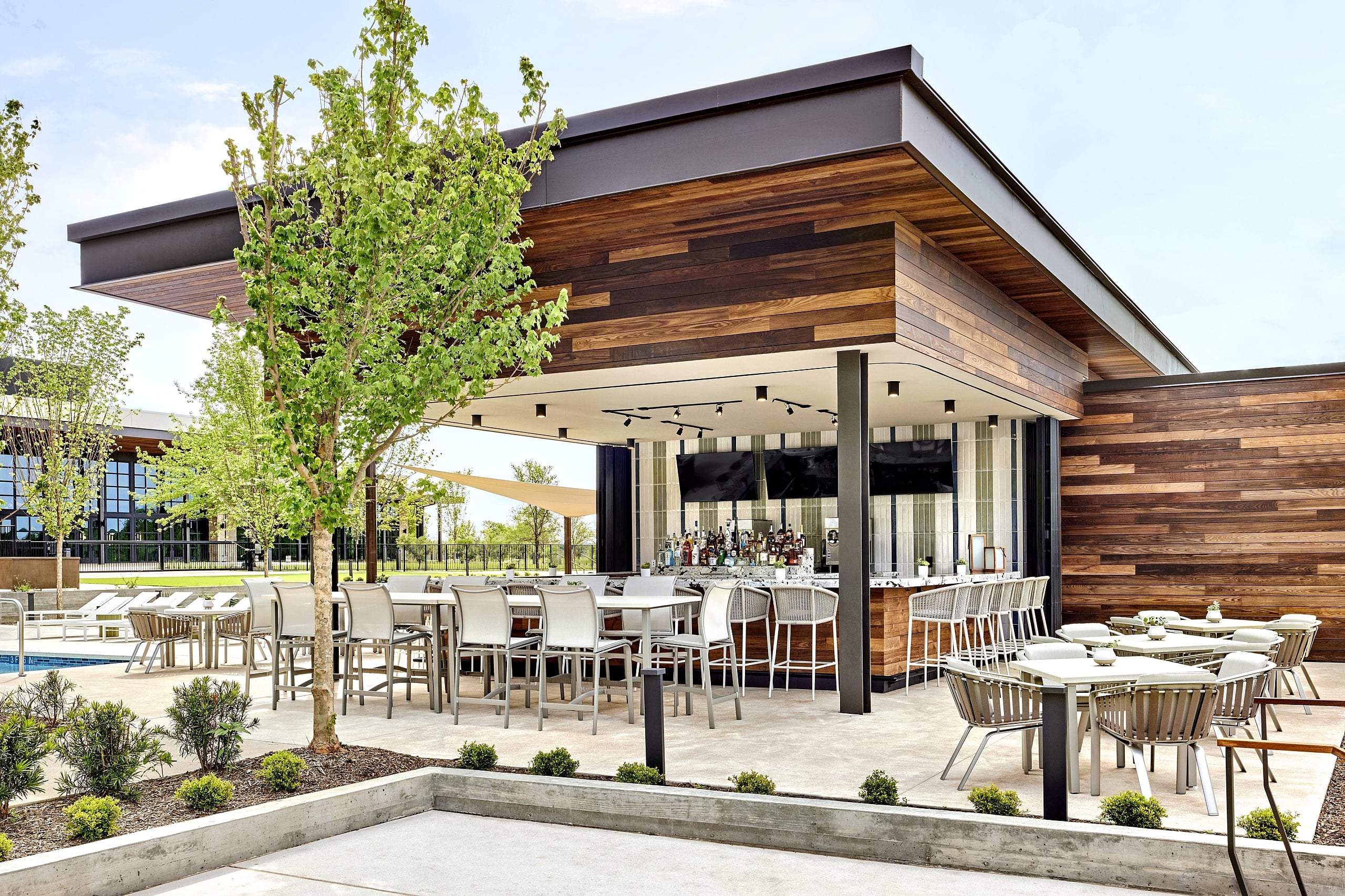 The outdoor Leisure Pool Bar at Omni PGA Frisco Resort, featuring modern wood paneling, a fully stocked bar, and contemporary outdoor seating and dining areas.