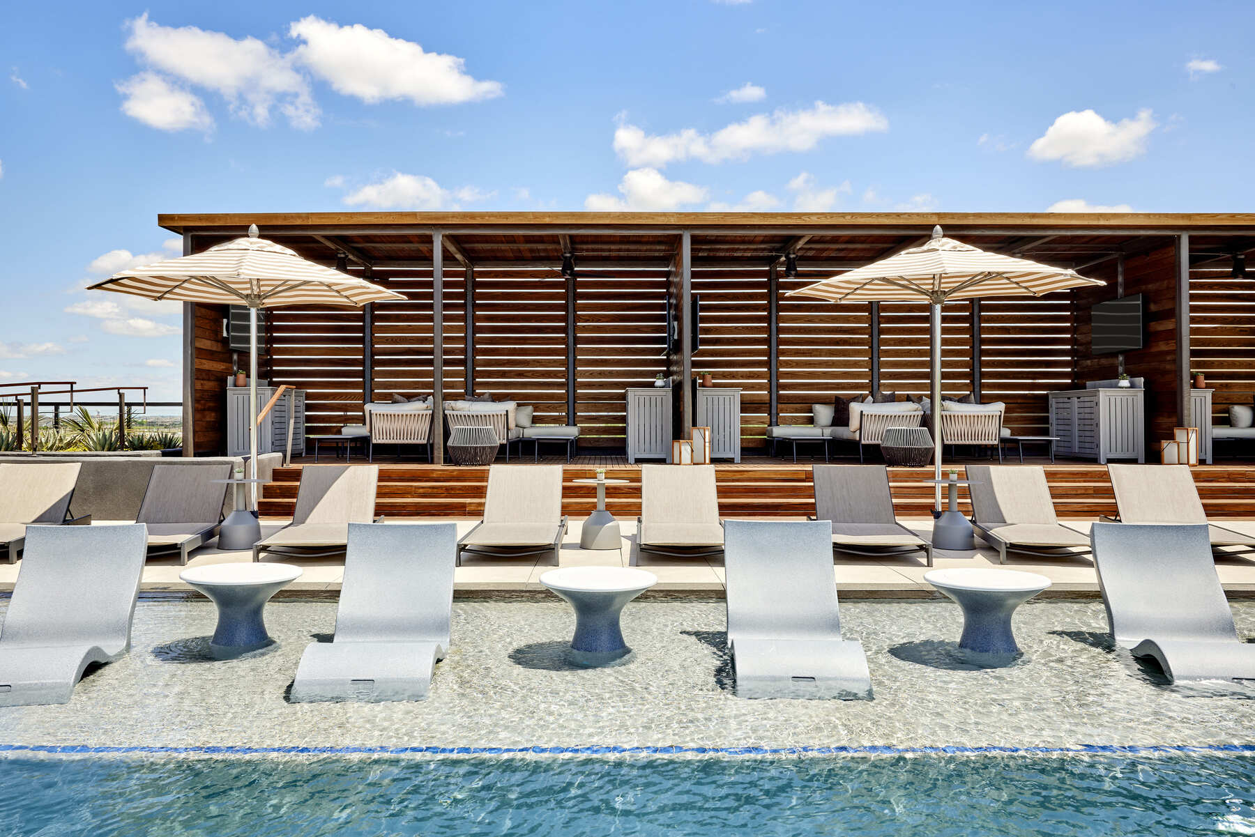 The adults-only rooftop pool cabanas at the Omni PGA Frisco Resort, showing modern wood-slat cabanas and in-pool lounge chairs.