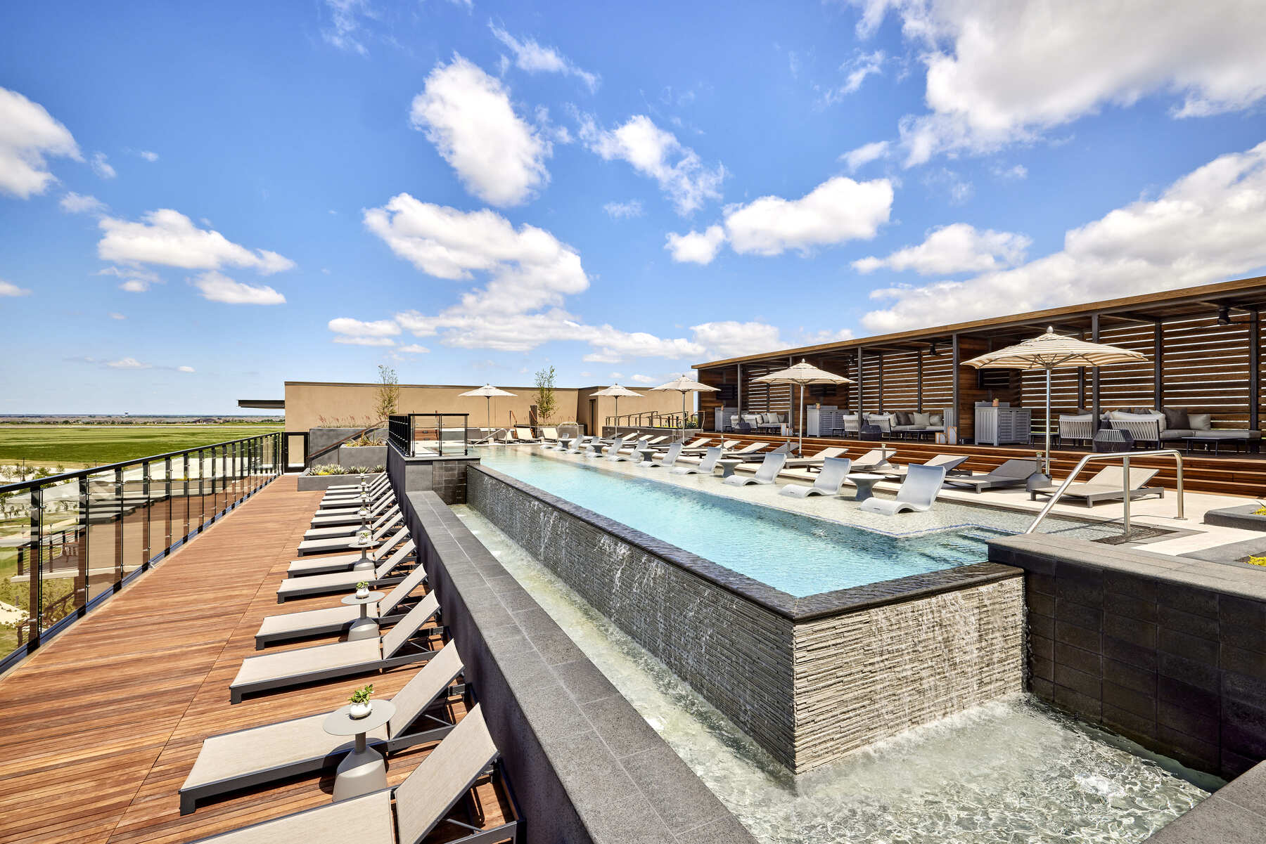 Panoramic view of the adults-only rooftop pool at the Omni PGA Frisco Resort, with a sleek infinity edge and wood decking under a blue sky.