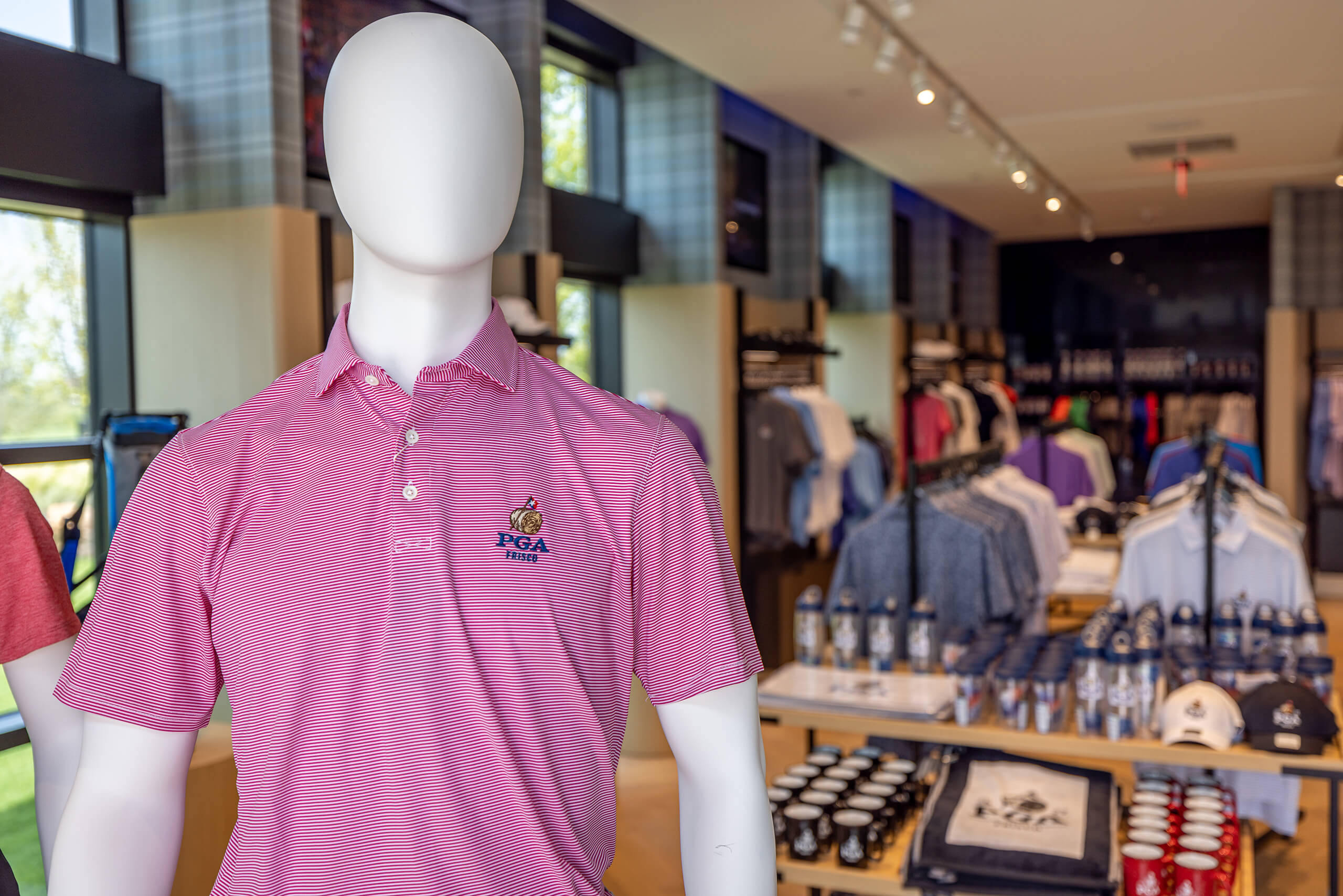Close-up of a mannequin in a retail store wearing a pink striped polo shirt embroidered with the PGA Frisco logo.