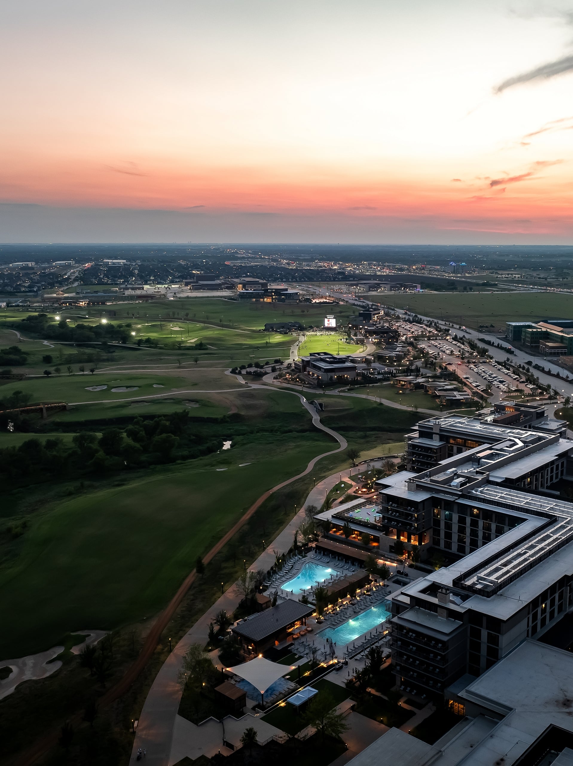 Aerial view of the Omni PGA Frisco Resort complex, showing the pools, buildings, and golf courses at dusk.