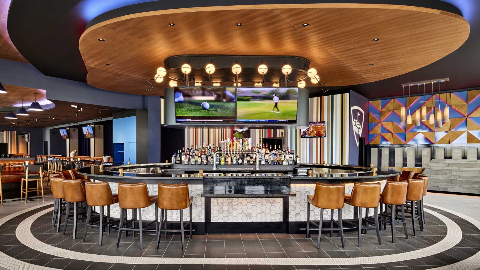 A circular bar in a modern sports lounge with leather stools, multiple screens showing golf, and a unique wood ceiling.