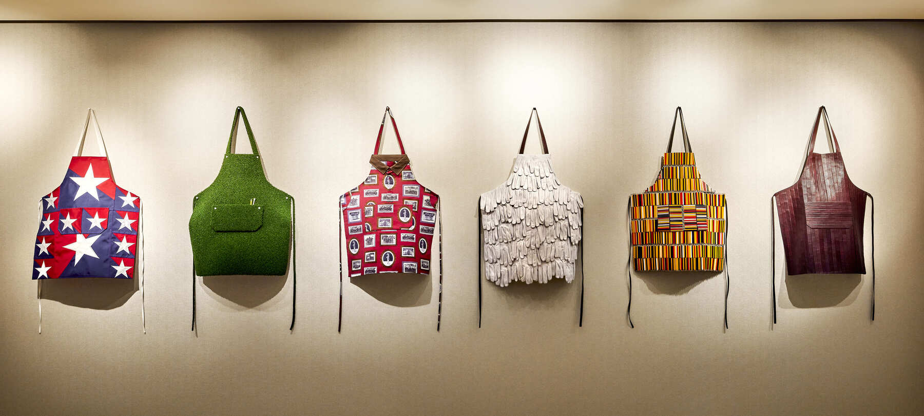 A decorative wall display featuring six artistic aprons with unique patterns and textures.