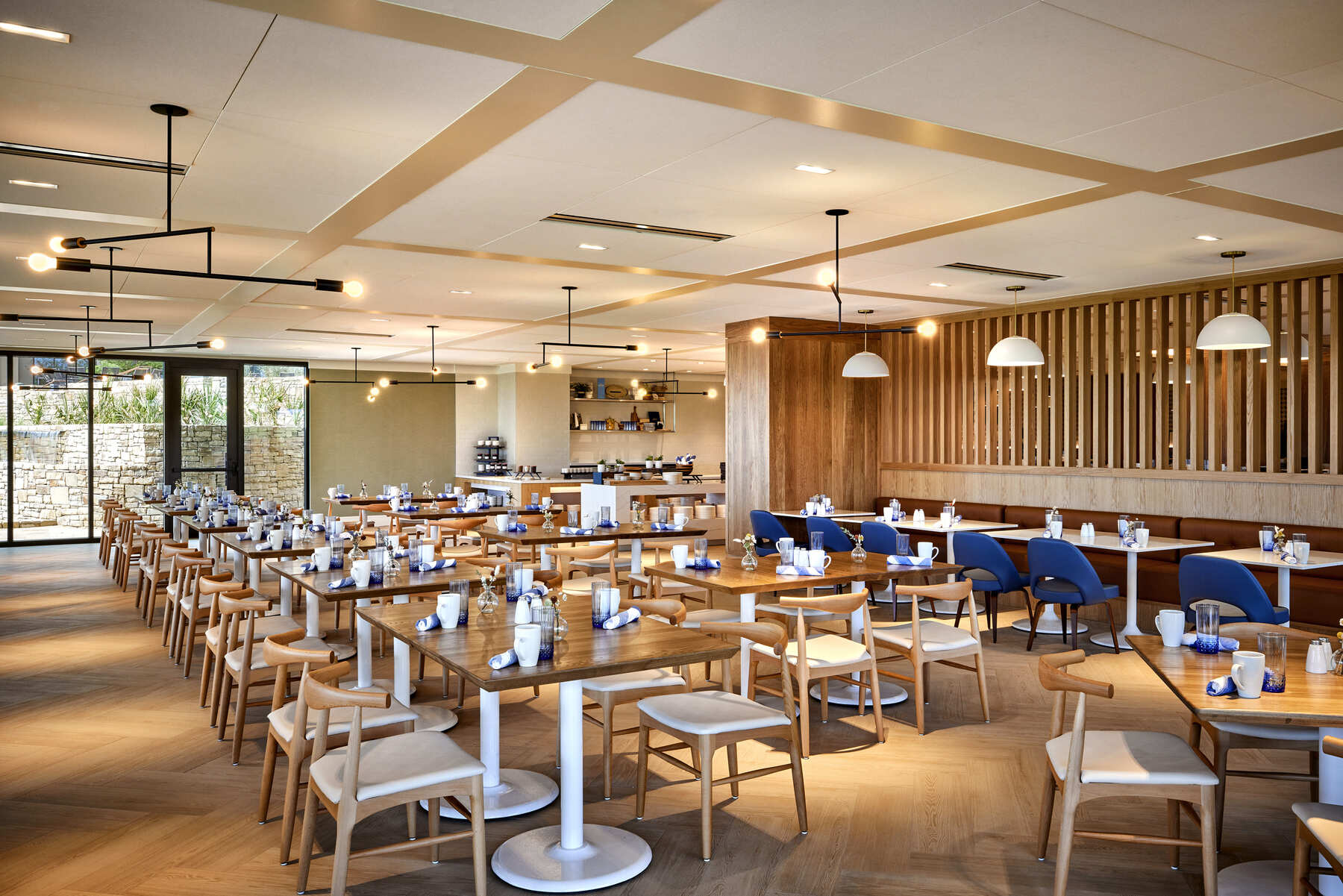 Modern, bright indoor dining room at The Apron Kitchen + Bar with wood tables and blue accent chairs.