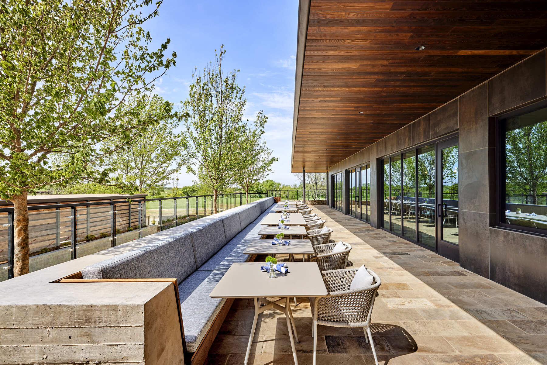 Outdoor patio dining area at The Apron Kitchen + Bar featuring cushioned bench seating and views of the grounds.