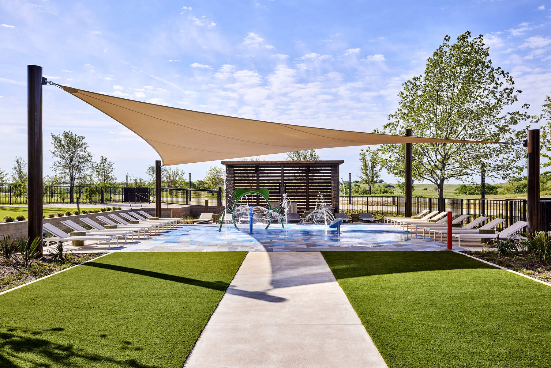 The Leisure Pool splash pad area at the Omni PGA Frisco Resort, featuring a water play area, lounge chairs, and a large triangular sun canopy.