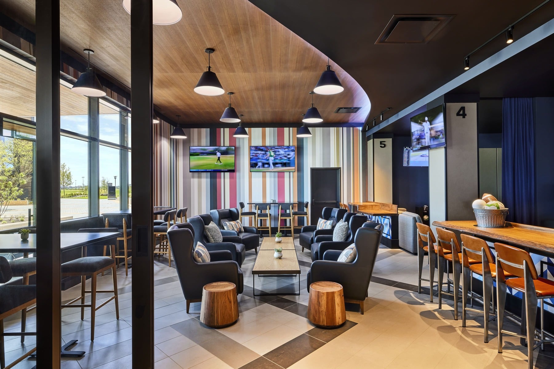 Interior of a Private Dining Room (PDR) within the Lounge by Topgolf, showing a casual lounge area with armchairs and small tables, and a bar area with TVs.