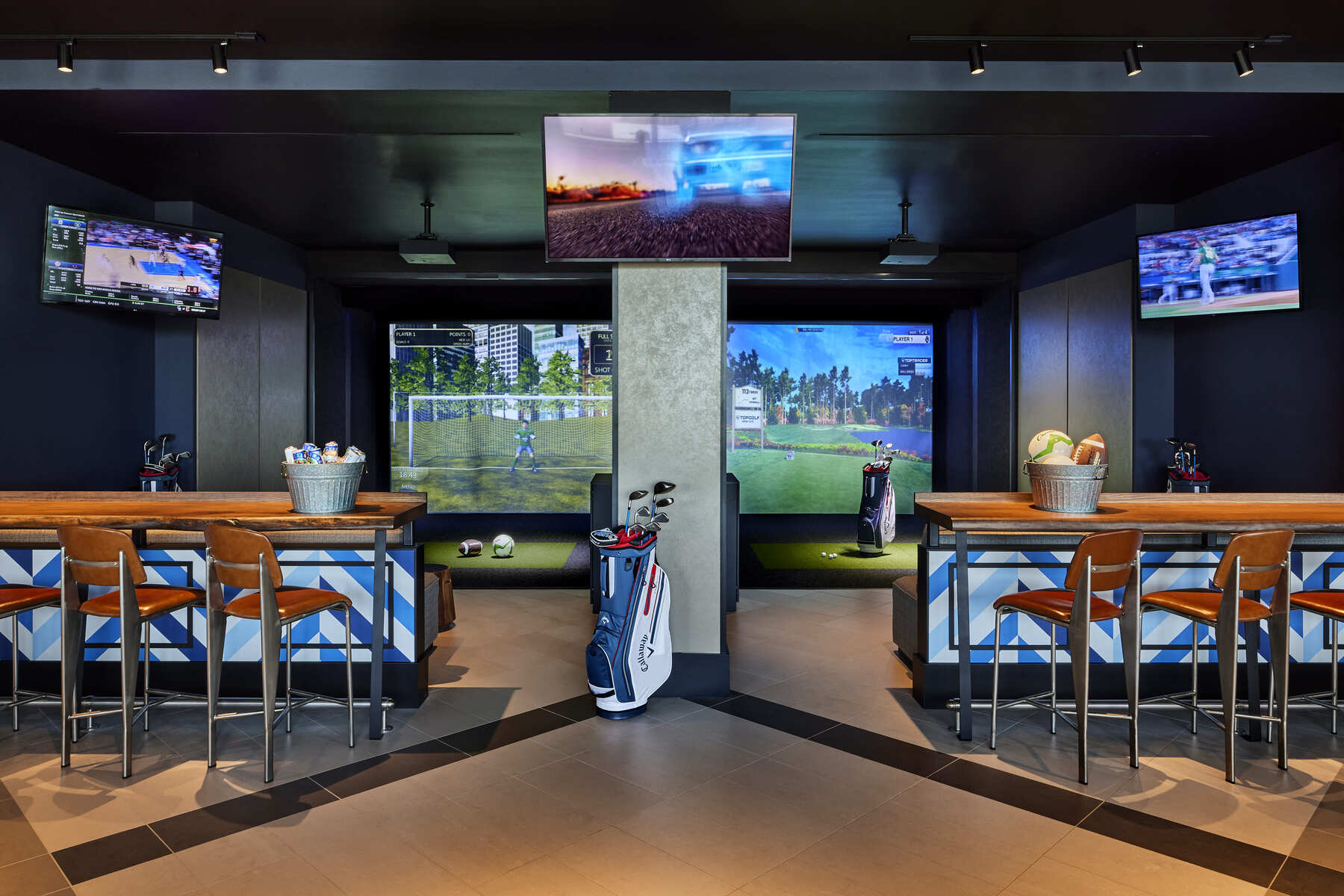The Lounge by Topgolf Swing Suite featuring two golf simulator screens, large TVs, high-top bars, and casual seating in a private entertainment area.