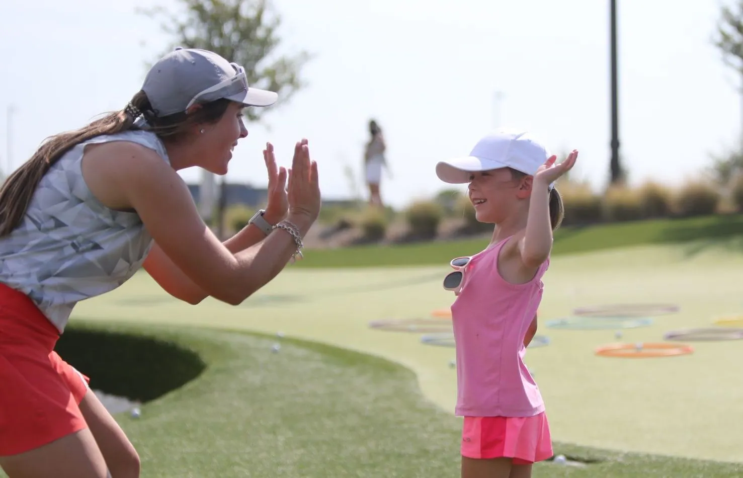 A woman coach and a young girl in golf gear high-five on a putting green during a lesson.