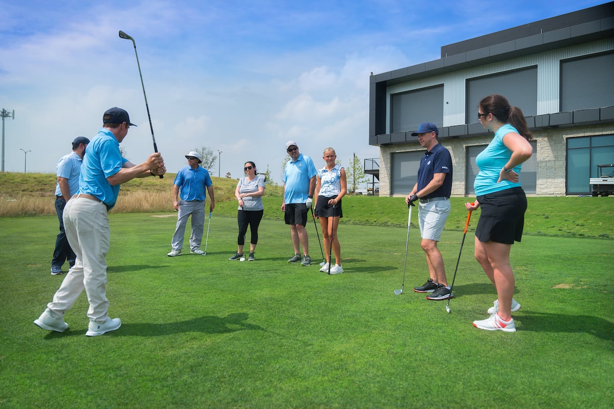 a group of golfers getting a lesson on a blue sky day