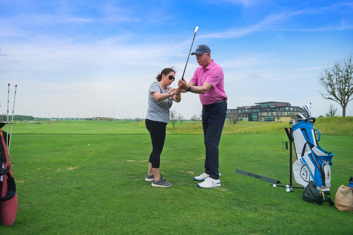 a golf coach guiding a student through their golf swing on a blue sky day