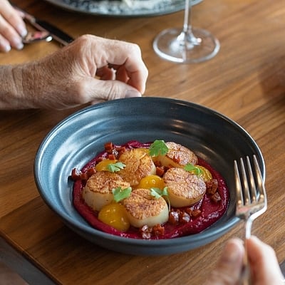 Close-up of a dark blue bowl containing five seared scallops on a bed of vibrant magenta puree