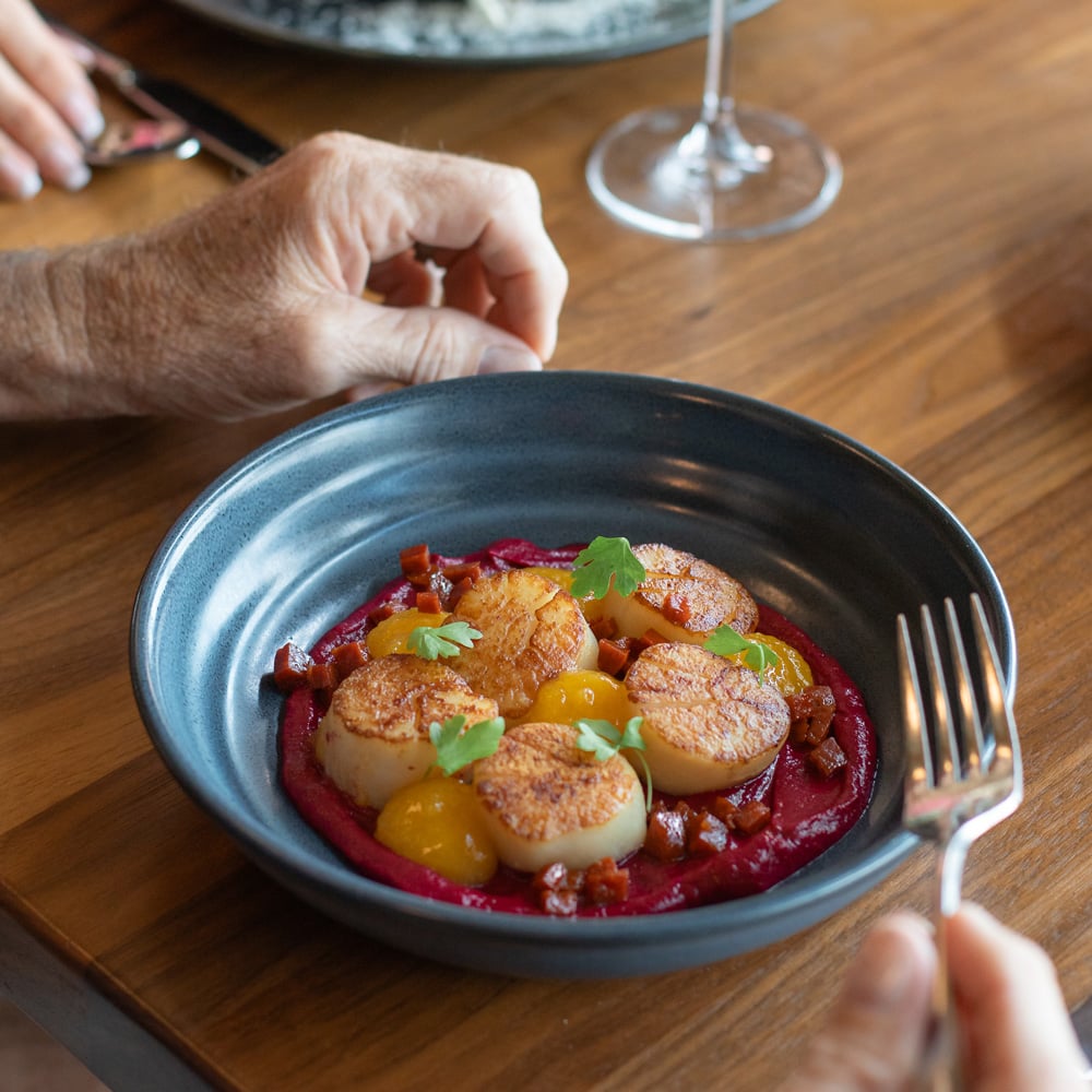 Close-up of a dark blue bowl containing five seared scallops on a bed of vibrant magenta puree