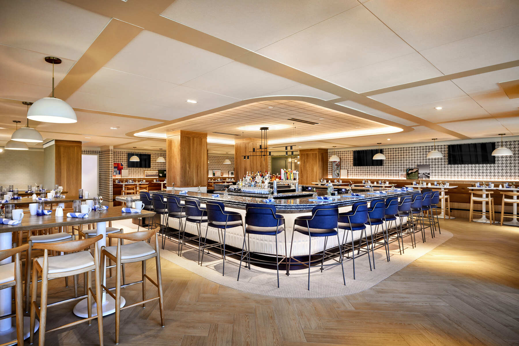Interior of the Ryder Cup Grille bar at Omni PGA Frisco, featuring light wood cabinetry, leather bar stools, and televisions above the liquor display.