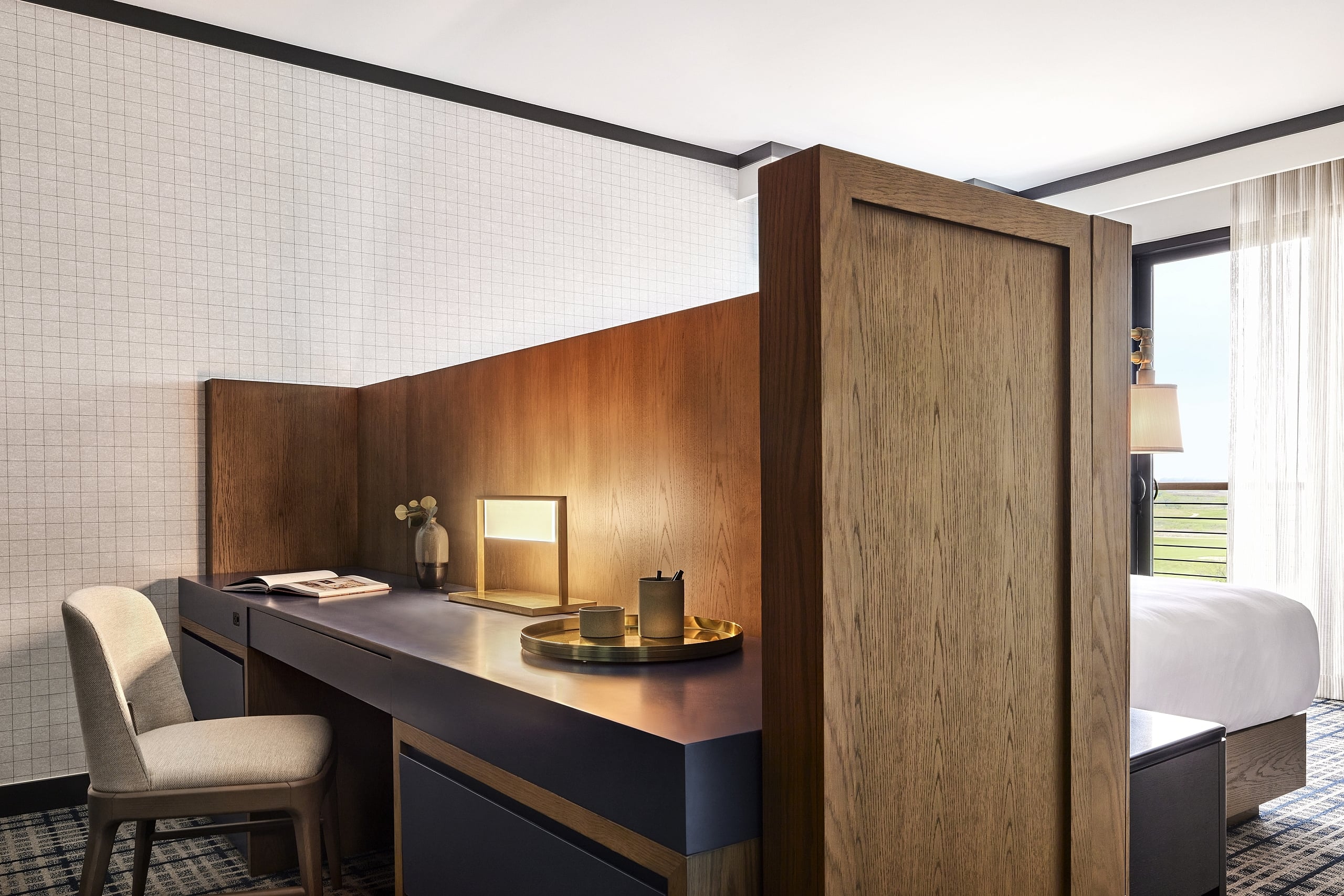 A dark wood desk/divider in a modern hotel room holds a lamp and tray, separating the sleeping area from the main room.