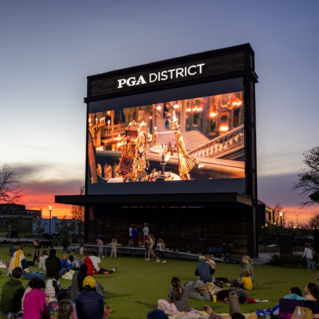 The screen at the PGA District displaying a movie as the sun sets in the background