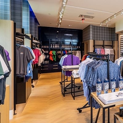 Interior view of a high-end golf pro shop featuring racks of colorful polo shirts and other apparel, with a dark blue accent wall and wood-style flooring.