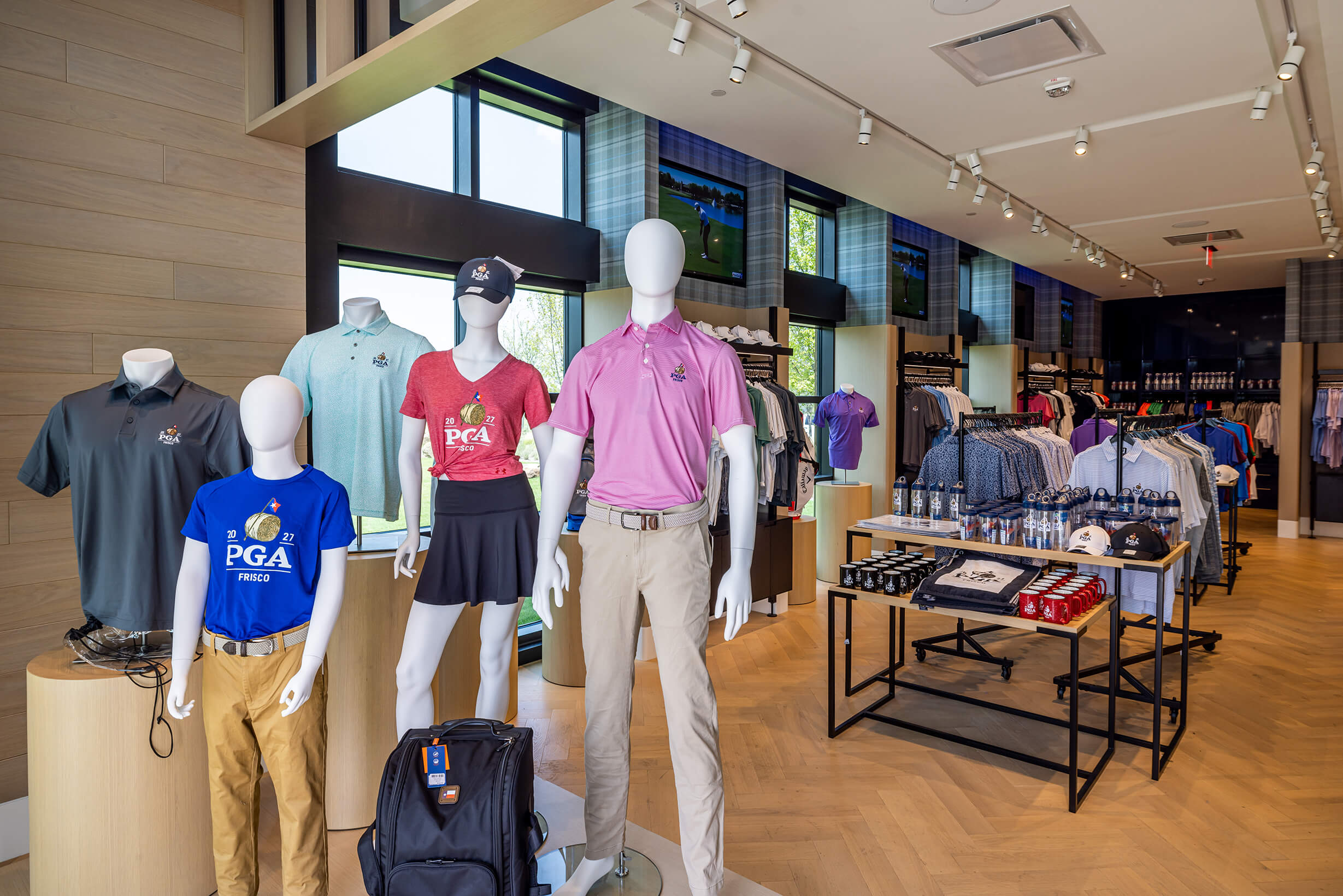Interior of a bright golf pro shop featuring mannequins displaying branded PGA Frisco apparel and racks of clothing.