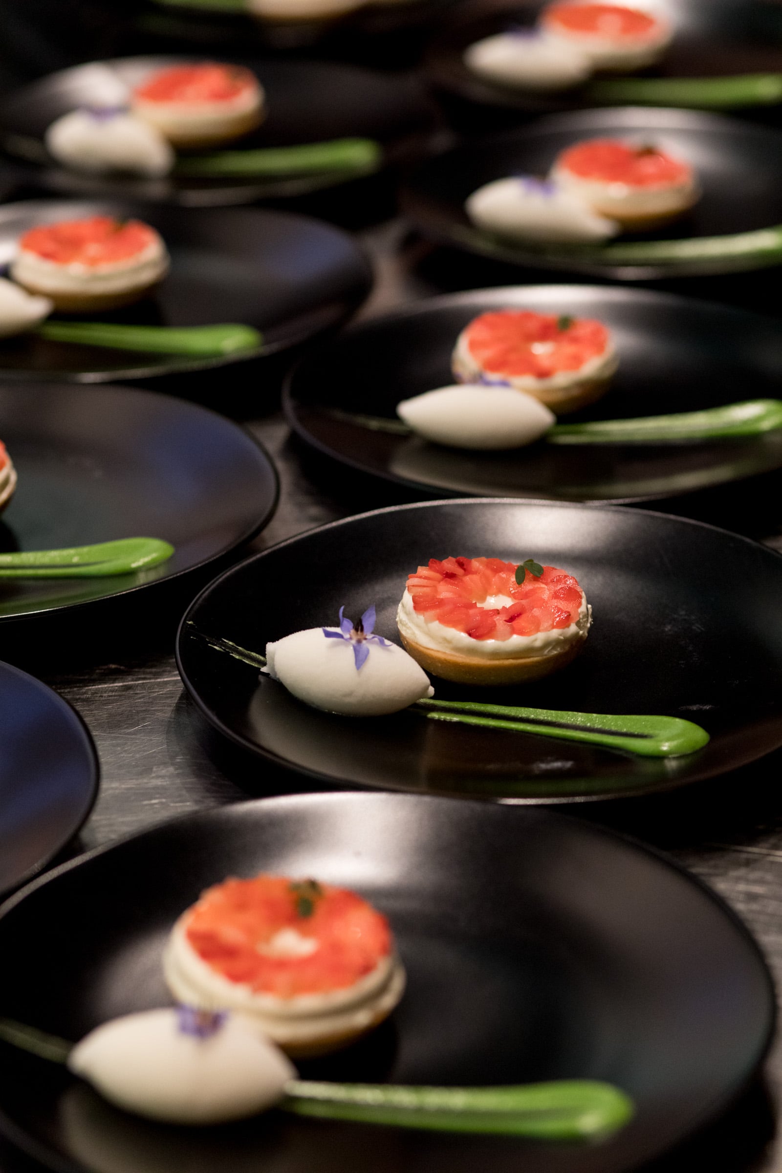 Rows of elegant plated desserts featuring a fruit-topped tart, a scoop of white sorbet, and a green sauce drizzle.