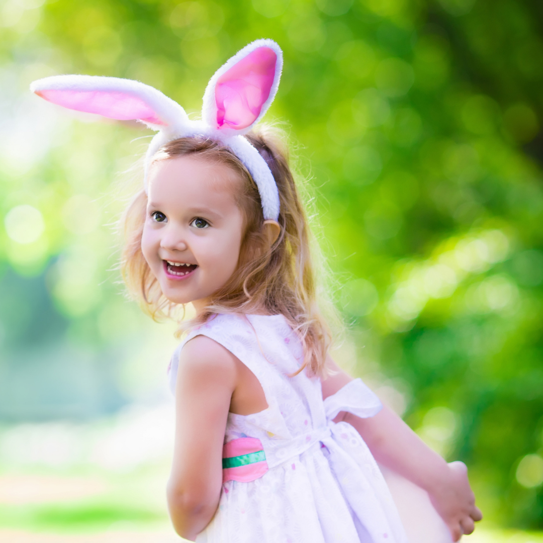A young girl wearing pink bunny ears laughing while playing outdoors on a sunny day.